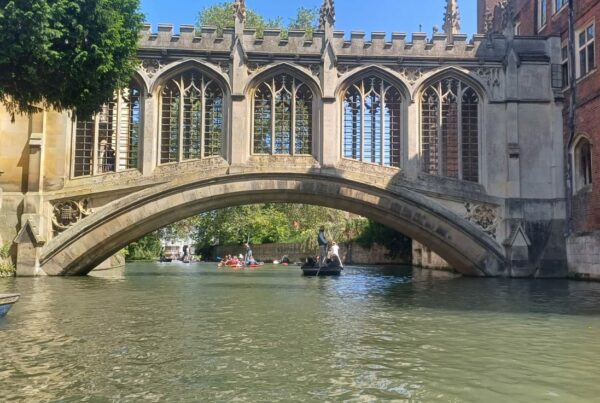 A bridge over water with people in boats Description automatically generated