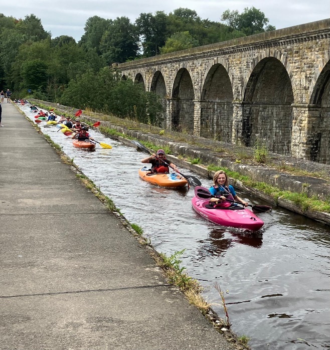 A group of people in kayaks on a canal

Description automatically generated