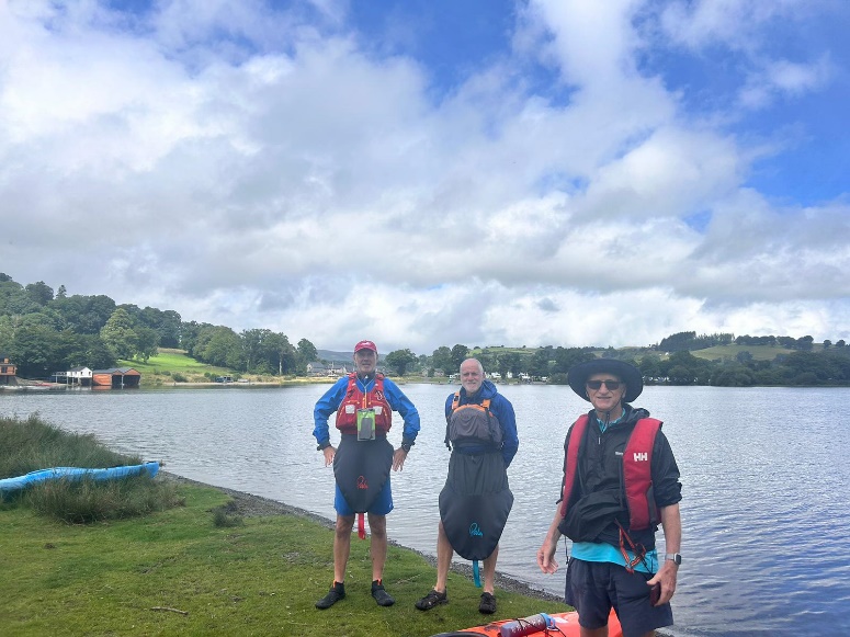 A group of people standing on grass next to a body of water

Description automatically generated